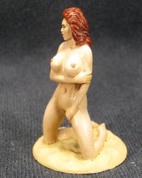 Erotic figurine of a naked woman, kneeling on the sand.