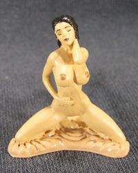 Erotic figurine of a naked female, kneeling on the pink silk sheet.